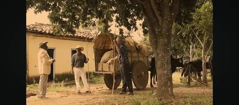 Cena de Venerável: carro de boi numa estrada de terra, ao lado de uma casa antiga